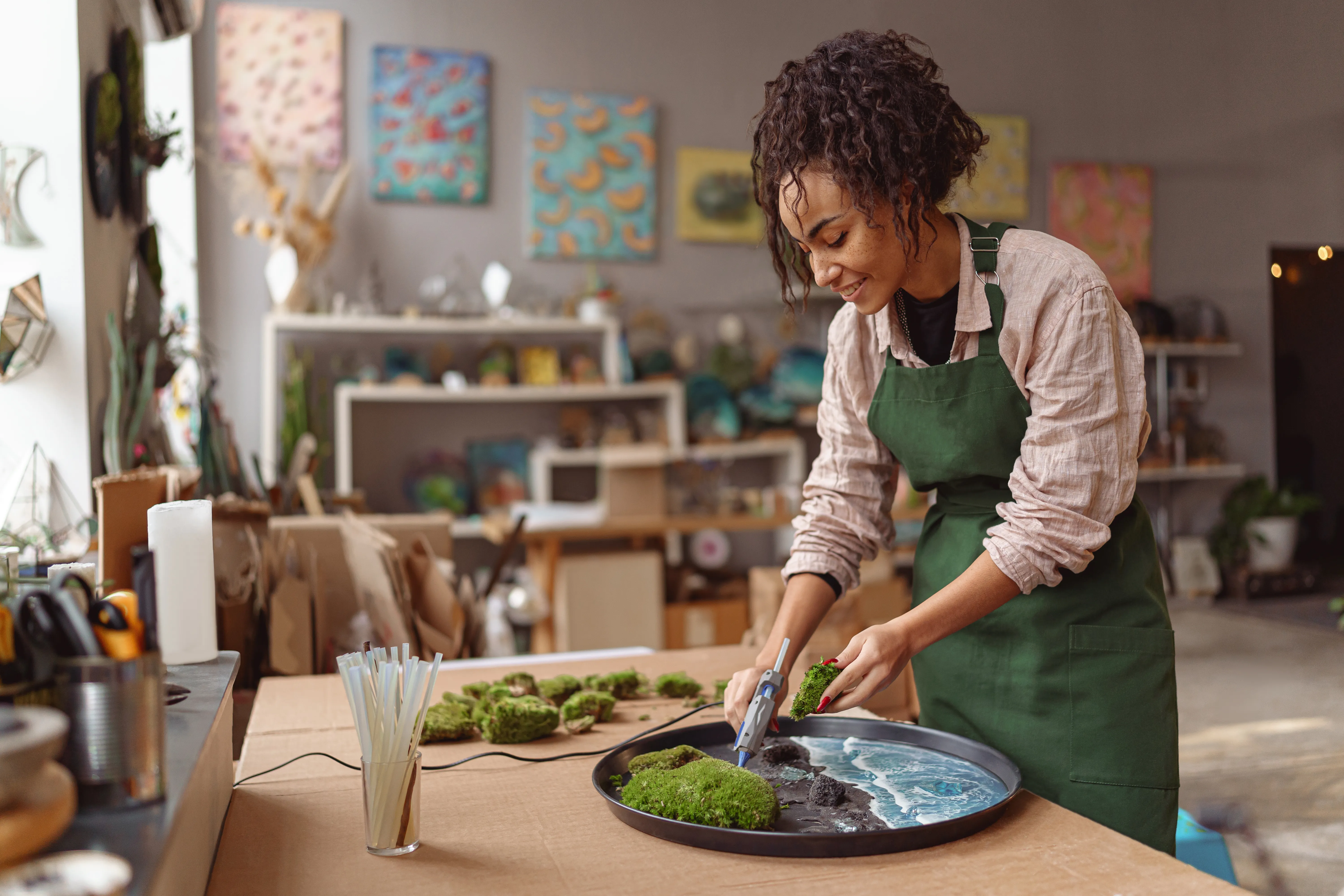 Se aprecia a una mujer sonriente haciendo ikebana verde en bandeja con resina epoxi en taller de floristería